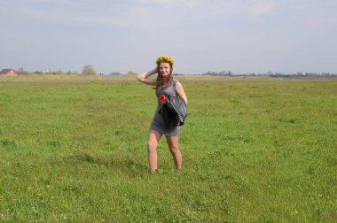 Bir çelenk dandelions başının üzerinde bir kızla yeşil alan yürür.