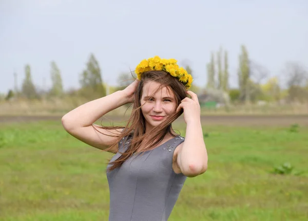 En flicka med en krans av maskrosor på hennes huvud. Vacker älva ung flicka i ett fält bland blommorna av tulpaner. — Stockfoto