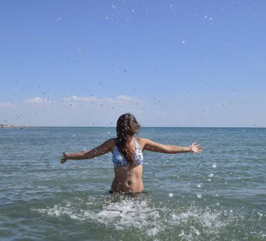 Deniz suyu içinde sprinkles. Uçan sprey su kadar atar. Kız siyah saçlı ve bir banyo ile deniz hoşlanır.