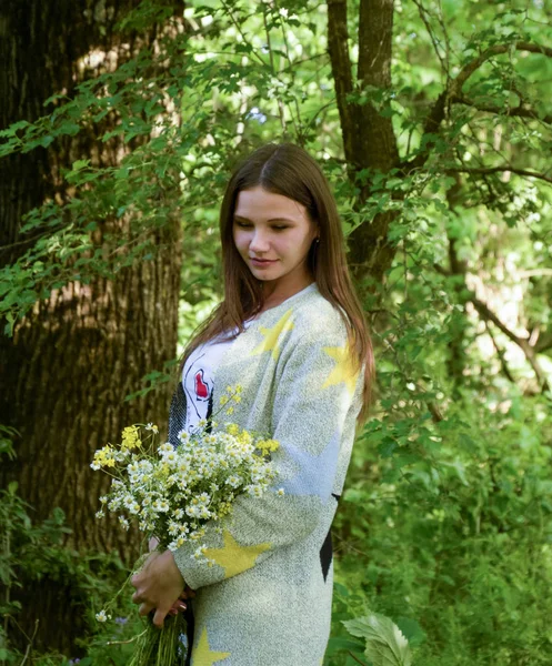 Jovem mulher bonita está de pé na floresta com um buquê de camomilas — Fotografia de Stock