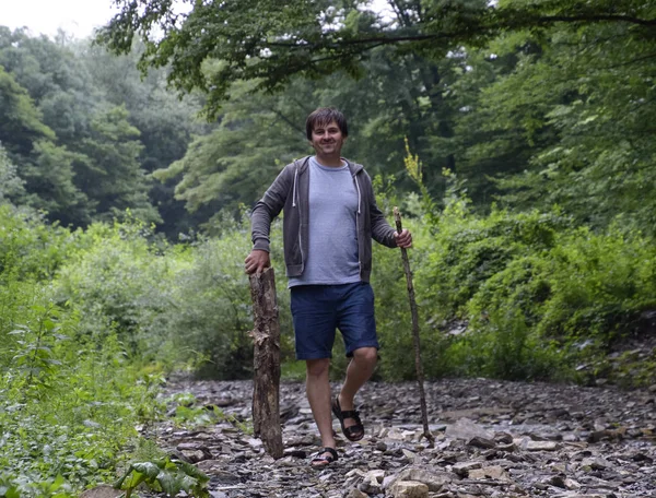 A man walks along the creek and carries wood for the fire. Picnic in nature. Harvesting of firewood.