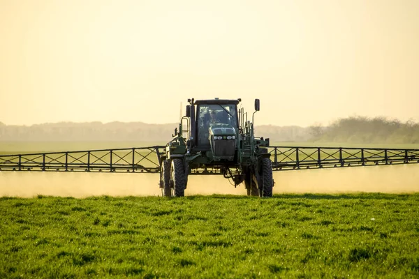 Ciągnik na tle zachodu słońca. Ciągnik z kołami o dużej jest Dokonywanie nawóz na młodej pszenicy. Stosowania drobno rozproszone spray chemikaliów — Zdjęcie stockowe