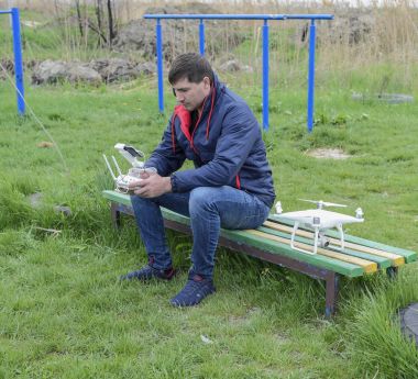 Uzaktan kumanda quadroopter onun elinde olan bir adam bir bankta oturuyor. Beyaz quadroopter hazırlamak için uçuş.