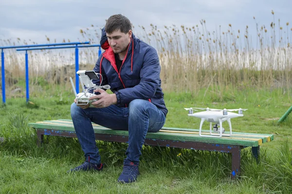 Uzaktan kumanda quadroopter onun elinde olan bir adam bir bankta oturuyor. Beyaz quadroopter hazırlamak için uçuş.