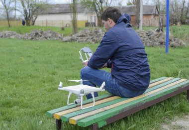 Uzaktan kumanda quadroopter onun elinde olan bir adam bir bankta oturuyor. Beyaz quadroopter hazırlamak için uçuş