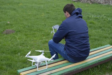 Uzaktan kumanda quadroopter onun elinde olan bir adam bir bankta oturuyor. Beyaz quadroopter hazırlamak için uçuş