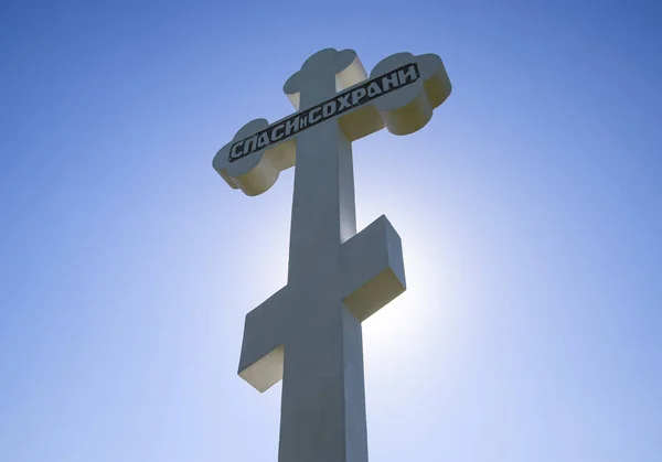 Pravoslavný kříž proti modrá obloha a slunce. Kříž v podsvícení slunce. Symbol křesťanské víry. Nápis na kříži: Záchrana a uchování — Stock fotografie