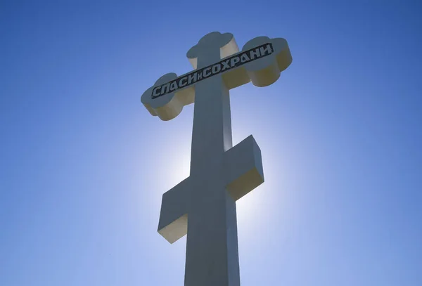 Orthodox cross against the blue sky and the sun. Cross in the backlight of the sun. Symbol of the Christian faith. The inscription on the cross: salvation and preservation — Stock Photo, Image