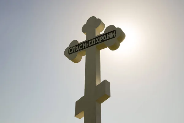 Pravoslavný kříž proti modrá obloha a slunce. Kříž v podsvícení slunce. Symbol křesťanské víry. Nápis na kříži: Záchrana a uchování — Stock fotografie