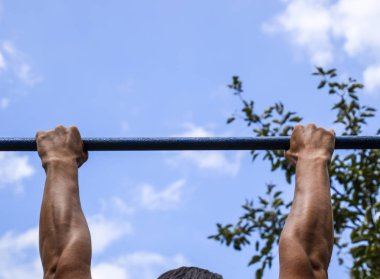 Çubuğunda eller yakın çekim. Adam kendini çubuğunda çeker. Temiz havada spor oynarken. Yatay çubuk