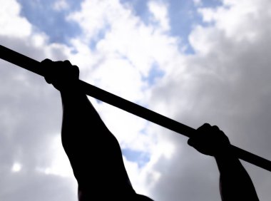 Yatay bir çubuk ellerde silüeti. Çubuğunda eller yakın çekim. Adam kendini çubuğunda çeker. Temiz havada spor oynarken. Yatay çubuk