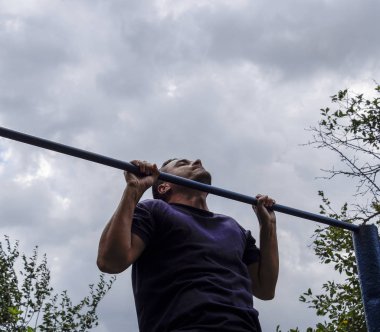 Adam kendini barın üzerine çekti. Temiz havada spor yapmak için. Yatay çubuk