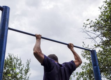 Adam kendini barın üzerine çekti. Temiz havada spor yapmak için. Yatay çubuk