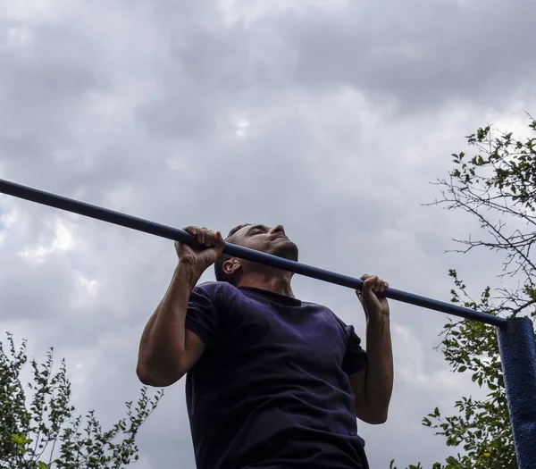 Adam kendini barın üzerine çekti. Temiz havada spor yapmak için. Yatay çubuk