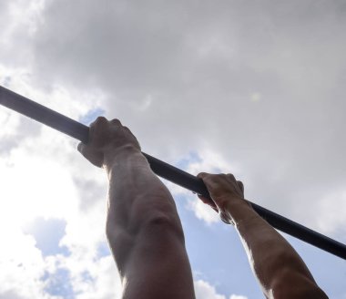 Çubuğunda eller yakın çekim. Adam kendini çubuğunda çeker. Temiz havada spor oynarken. Yatay çubuk