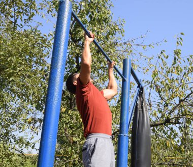 Adam kendini çubuğunda çeker. Temiz havada spor oynarken. Bahçedeki ev yapımı yatay çubuk