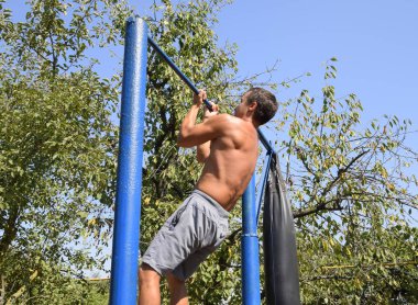 Adam kendini çubuğunda çeker. Temiz havada spor oynarken. Bahçedeki ev yapımı yatay çubuk