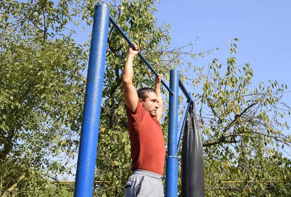 Adam kendini çubuğunda çeker. Temiz havada spor oynarken. Bahçedeki ev yapımı yatay çubuk
