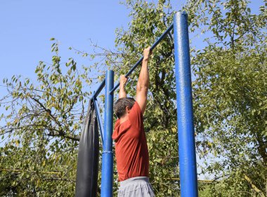 Adam kendini çubuğunda çeker. Temiz havada spor oynarken. Bahçedeki ev yapımı yatay çubuk