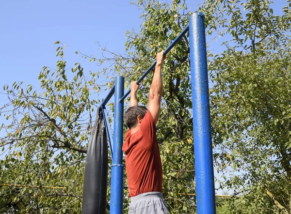 Adam kendini çubuğunda çeker. Temiz havada spor oynarken. Bahçedeki ev yapımı yatay çubuk