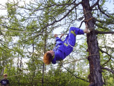 Bir turist kızın ağaçları arasında bir ip tırmanıyor.
