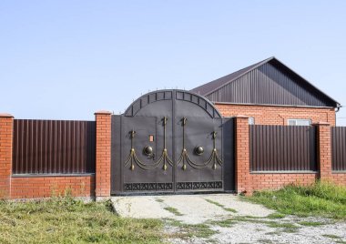 Bir çit ve gates ile tuğla ev. Görünümü yeni bir İnşaatlı çit ve tuğla ve oluklu metal yapılmış bir ev