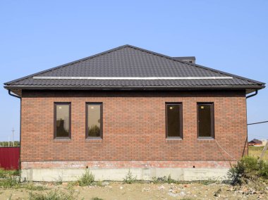 Plastik pencere ve oluklu levha çatısı olan ev. Kahverengi çatı ve kahverengi tuğla