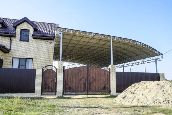 Bir çit ve gates ile tuğla ev. Çelik çerçeve ile büyük bir tente. Görünümü yeni bir İnşaatlı çit ve tuğla ve oluklu metal yapılmış bir ev