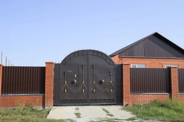 Bir çit ve gates ile tuğla ev. Görünümü yeni bir İnşaatlı çit ve tuğla ve oluklu metal yapılmış bir ev.