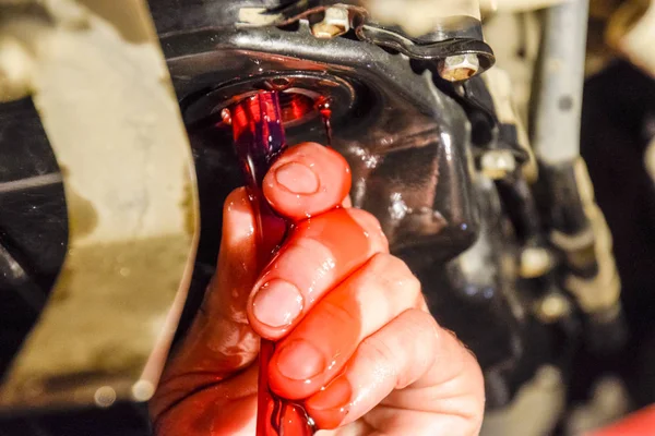 Oil change in automatic transmission. Filling the oil through the hose. Car maintenance station. Red gear oil. The hands of the car mechanic in oil.