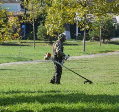 Krasnodar, Rusya - 12 Ekim 2016: bir işçi bir benzin fırça ile çim biçme. Düzeltici. Balık tutma çizgi düzeltici kullanarak yeşil çim biçme. Uygulama & bıyık kesme makineleri.