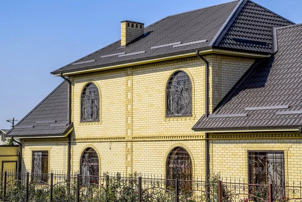 Huis van de gele baksteen en bruin golfplaten dak gemaakt van metaal. Roosters op de ramen. — Stockfoto