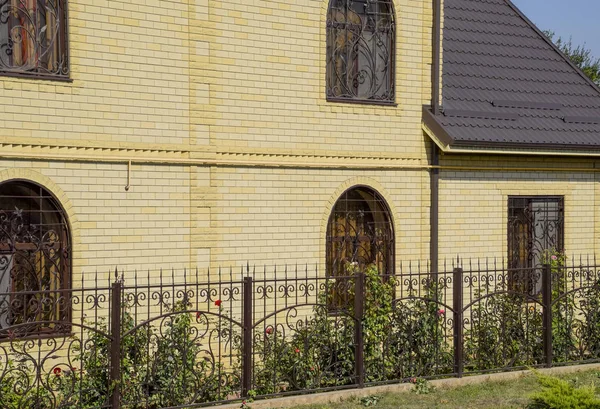Будинок з жовтого цегли і коричневого гофрованого даху з металу. Грати на вікнах . — стокове фото