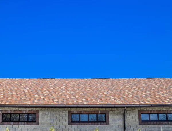 Дом выполнен из бежевого кирпича, крыша покрыта битумной черепицей. Металлические пластиковые окна на доме . — стоковое фото