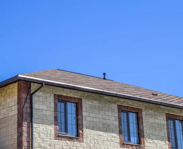 Das Haus besteht aus beigefarbenen Ziegeln, das Dach ist mit Bitumenschindeln gedeckt. Kunststoff-Metallfenster am Haus. — Stockfoto
