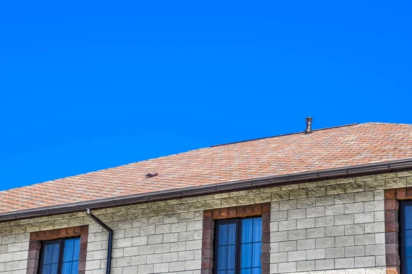 La maison est faite de briques beiges, le toit est couvert de bardeaux de bitume. Fenêtres en plastique métallique sur la maison . — Photo