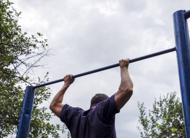 Adam kendini barın üzerine çekti. Temiz havada spor yapmak için. Yatay çubuk