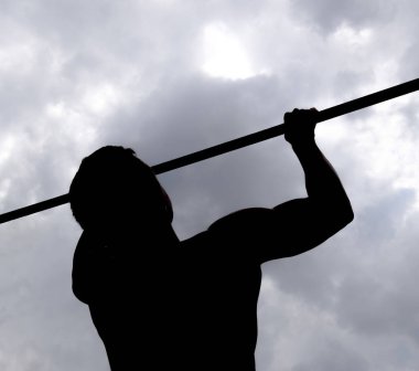 Bir atlet bir çubuğu silüeti. Adam kendini çubuğunda çeker. Temiz havada spor oynarken. Yatay çubuk