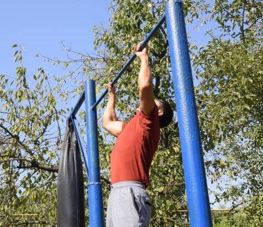 Adam kendini çubuğunda çeker. Temiz havada spor oynarken. Bahçedeki ev yapımı yatay çubuk