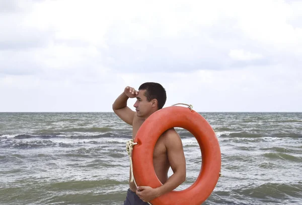 The man on the beach with a lifebuoy. Safety beach holiday at sea. Man with a life buoy on the beach. Rescue and safety on the water.