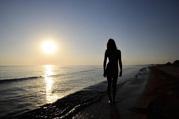 Silueta de una chica contra el atardecer junto al mar —  Fotos de Stock