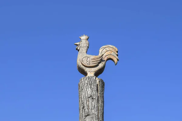 Figurine of a rooster on a tree stump on a background of blue sk — Stock Photo, Image