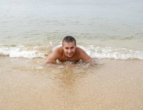 Человек на берегу лжет. Морская волна покрывает мужскую. пляж — стоковое фото