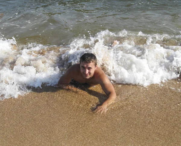 Man on the shore lies. The sea wave covers the masculine. Beach — Stock Photo, Image