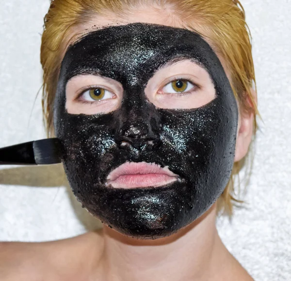 Chica con una máscara negra cosmética. Mascarilla limpiadora de aspirina y carbón activado. Mascarilla cosmética negra . — Foto de Stock