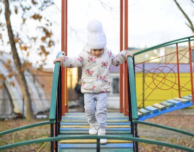 Little girl is playing on the playground in the park. The child goes on the steps of the playground. clipart