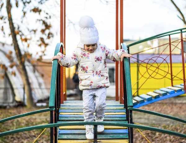 Little girl is playing on the playground in the park. The child goes on the steps of the playground