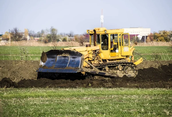 The yellow tractor with attached grederom makes ground leveling. Work on the drainage system in the field.