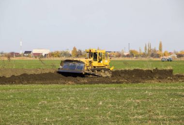 Sarı traktör ekli grederom ile zemin tesviye yapar. Drenaj sistemi alanında çalışmak.