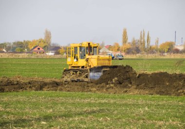 Sarı traktör ekli grederom ile zemin tesviye yapar. Drenaj sistemi alanında çalışmak.